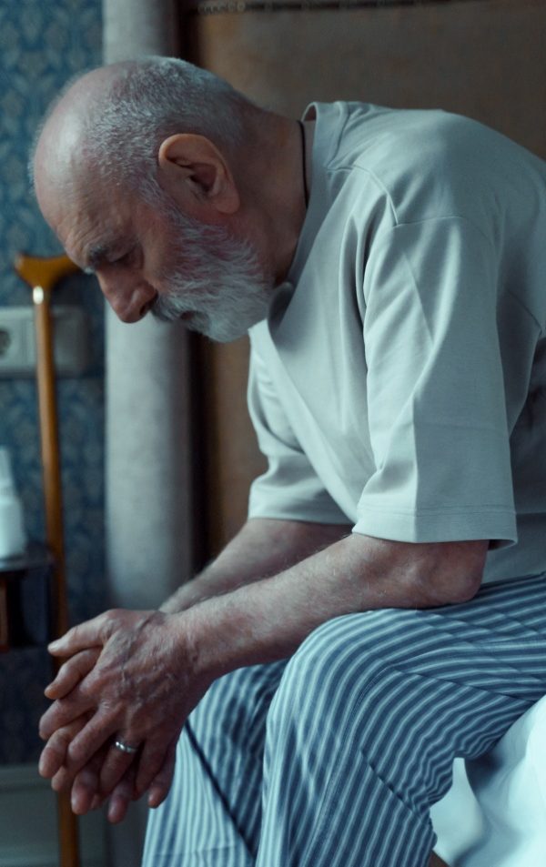 An old man sitting at the edge of a bed