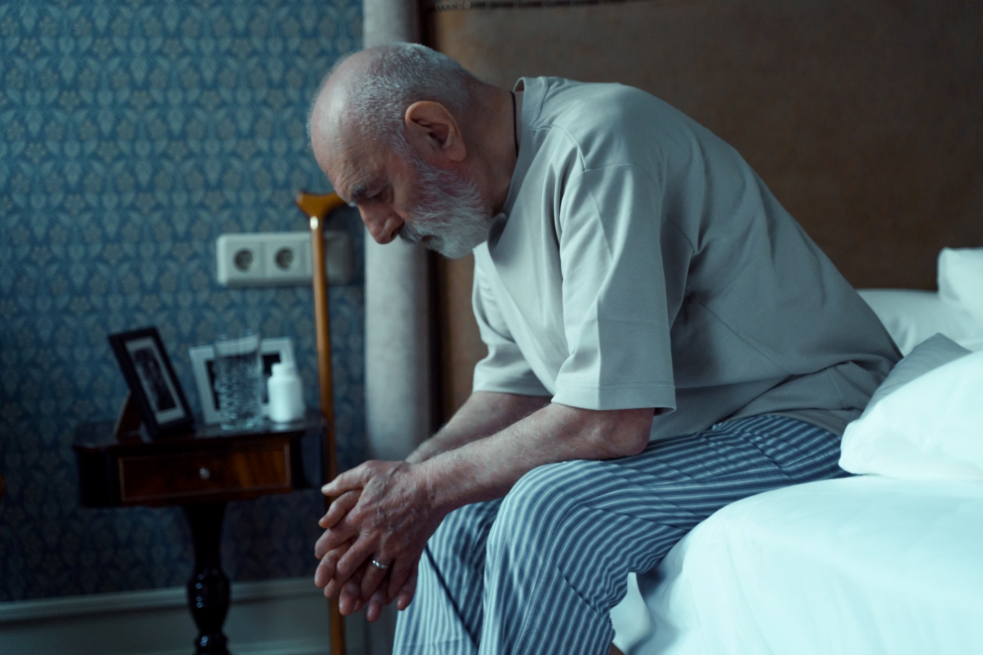 An old man sitting at the edge of a bed