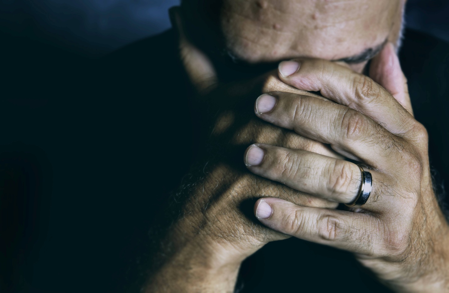 An older man covering his face with his hands